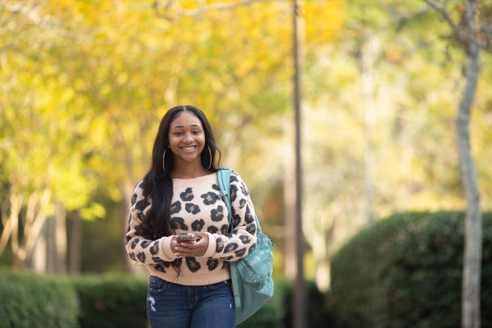 A student smiling surrounded by fall foliage.