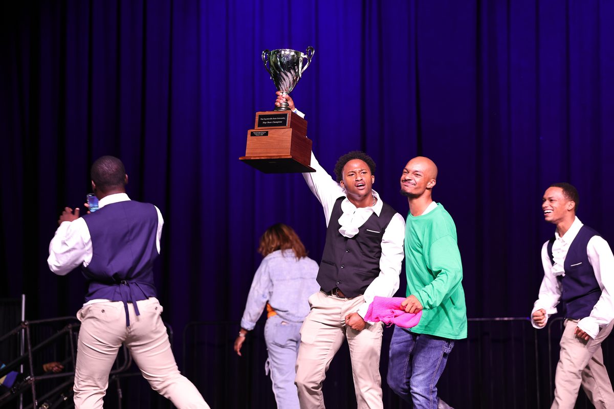 A fraternity member raises the Fayetteville State University Step Show Champions trophy as his chapter celebrates.