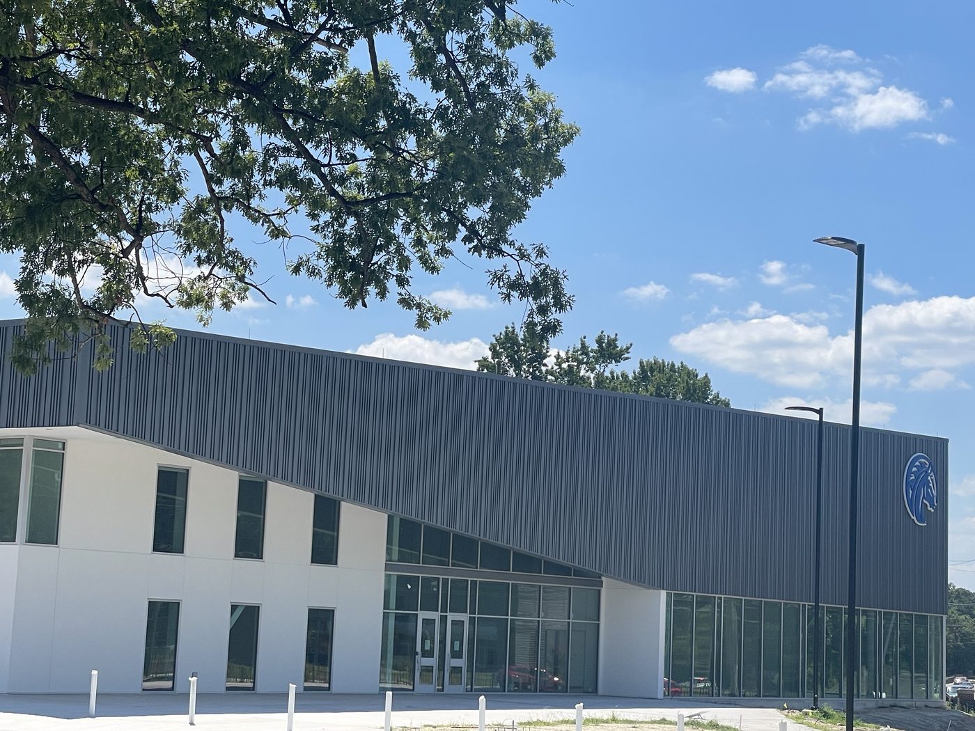 Photograph of the new FSU Health and Wellness Center nearing completion: a long two-story building with a dark ribbed metal upper level cantilevered over a white ground floor and a two-story glass entrance, under a clear sky.