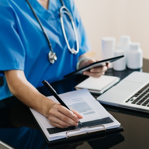 Someone in blue medical scrubs writing on a clipboard.