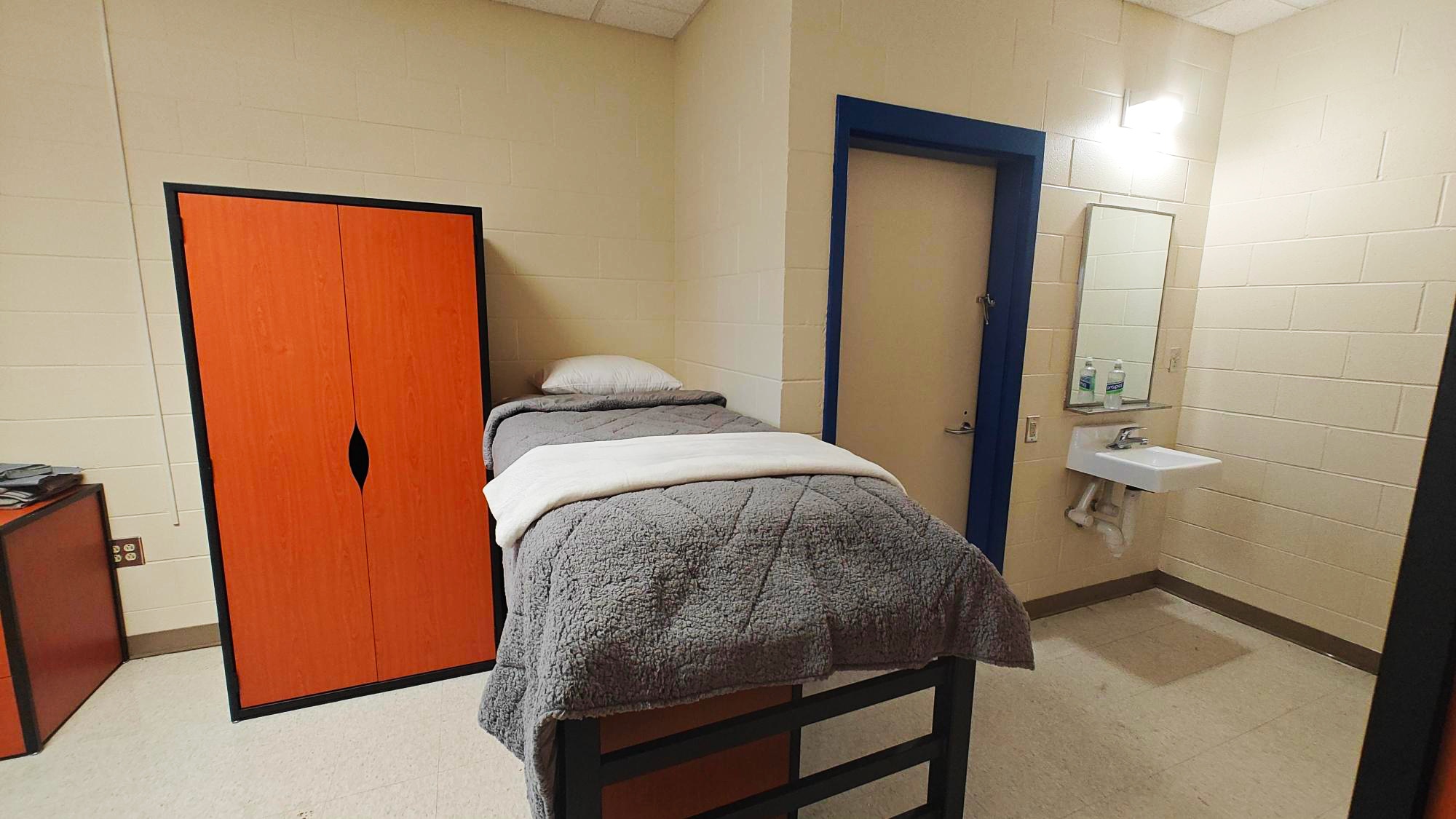 The same bedroom, the camera centered on a single bed. A sink is just in view.