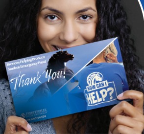 A Fayetteville State University student smiling while holding a Broncos Helping Broncos Student Emergency Fund thank-you card.