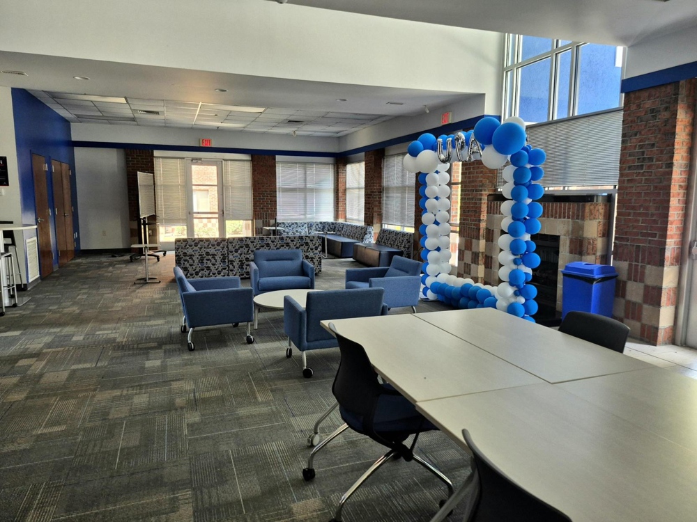 A carpetted lobby/common area with comfortable blue chairs and tables.