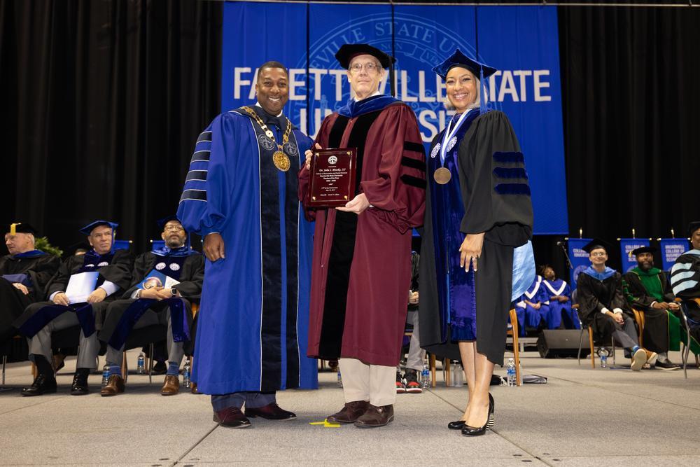 The Chancellor standing with two faculty members, holding an award.