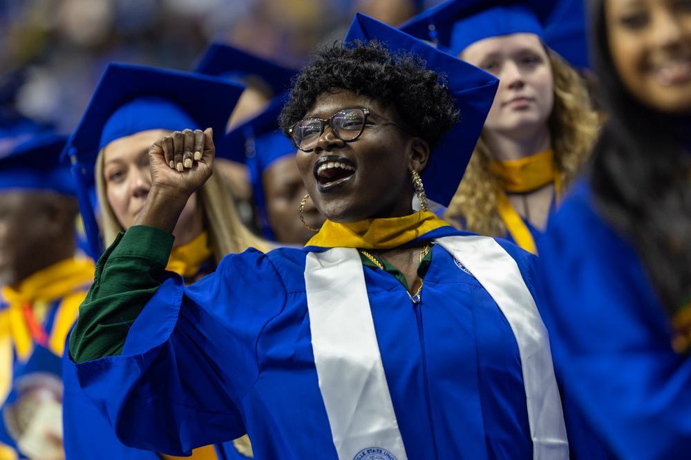 FSU student in a cap and gown cheering.