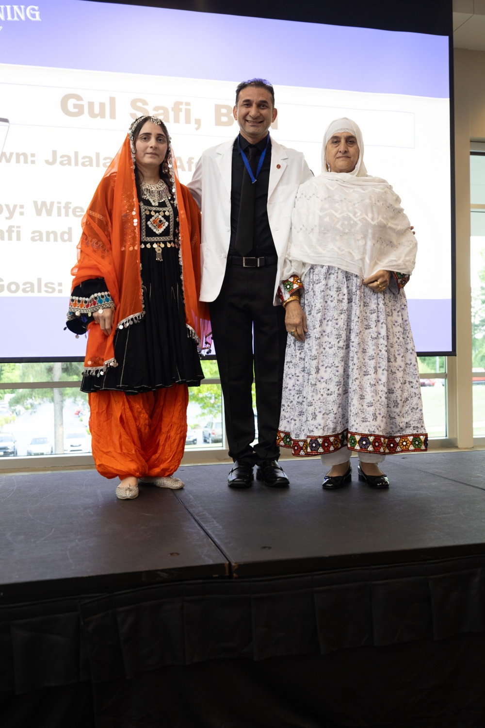 Gul Safi standing between two women, in front of a presentation.