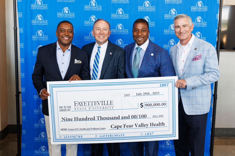 The chancelor surrounded by other distinguished individuals, holding a giant check.