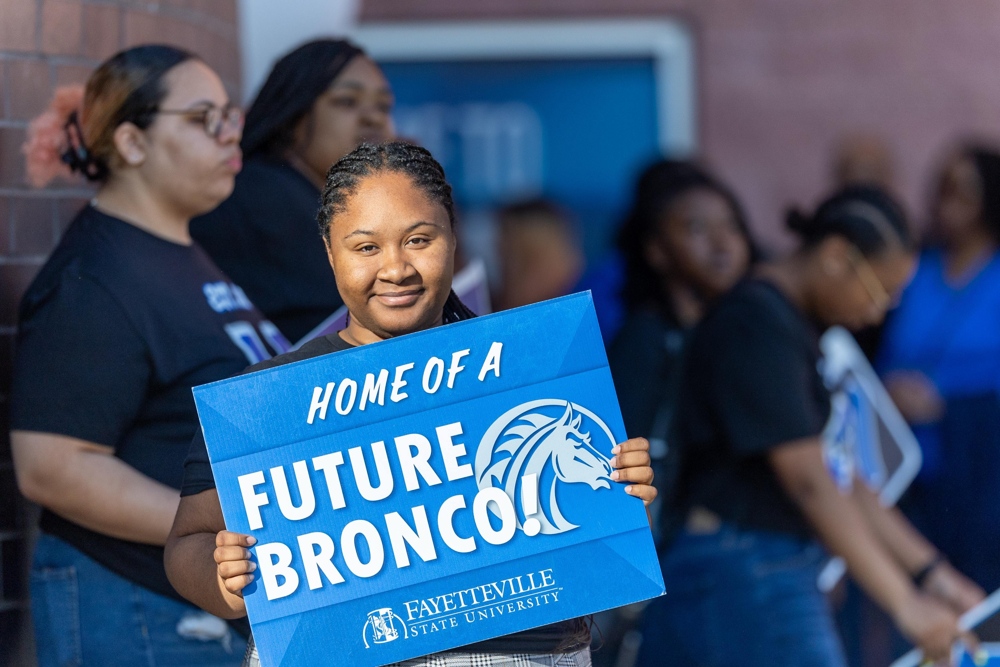 A student holding a sign saying: Home of a Future Bronco