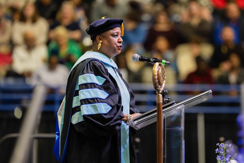 Monica Terrell Leach speaking at a podium in front of a crowd.