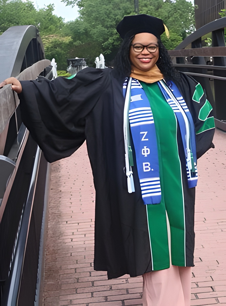 Mosley in a cap and gown, standing on a bridge.