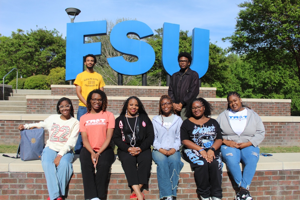 SeQuenna sitting on brick steps, with a number of students. The blue FSU sign can be seen in the background.