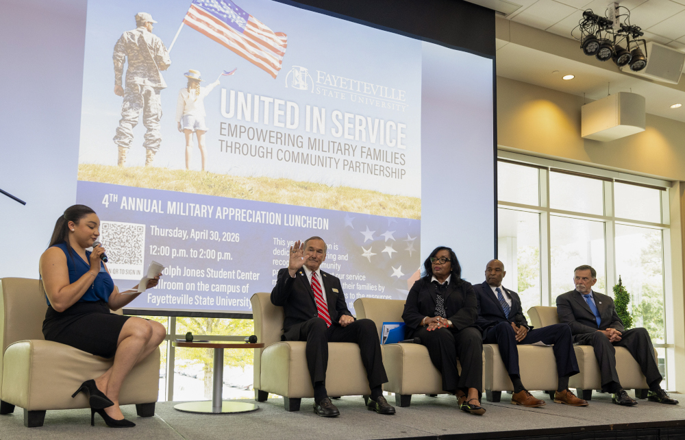 Speakers and a moderator on stage. An 'United in Service' banner can be seen behind them.