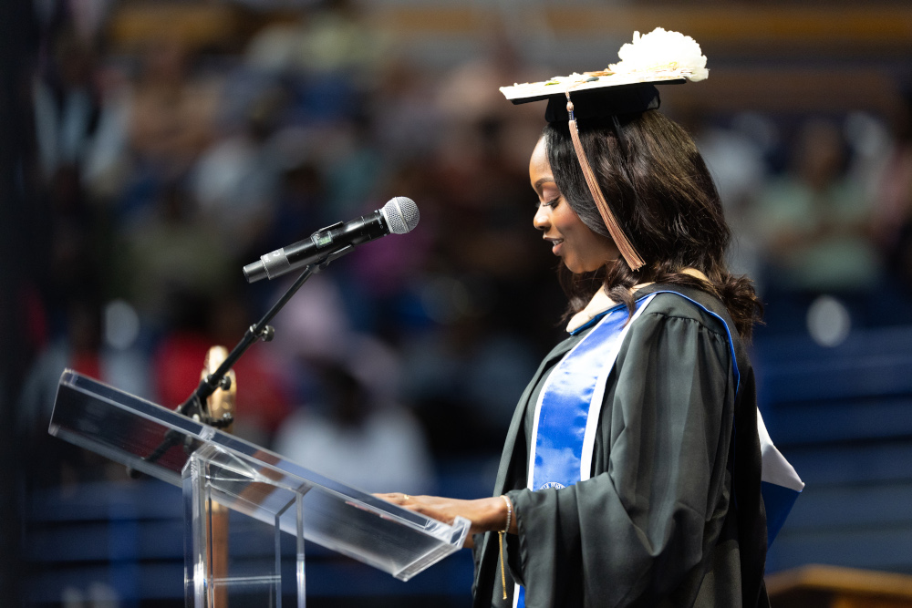 Sierra Osborn, standing behind a podium in front of a crowd, wearing a cap and gown.