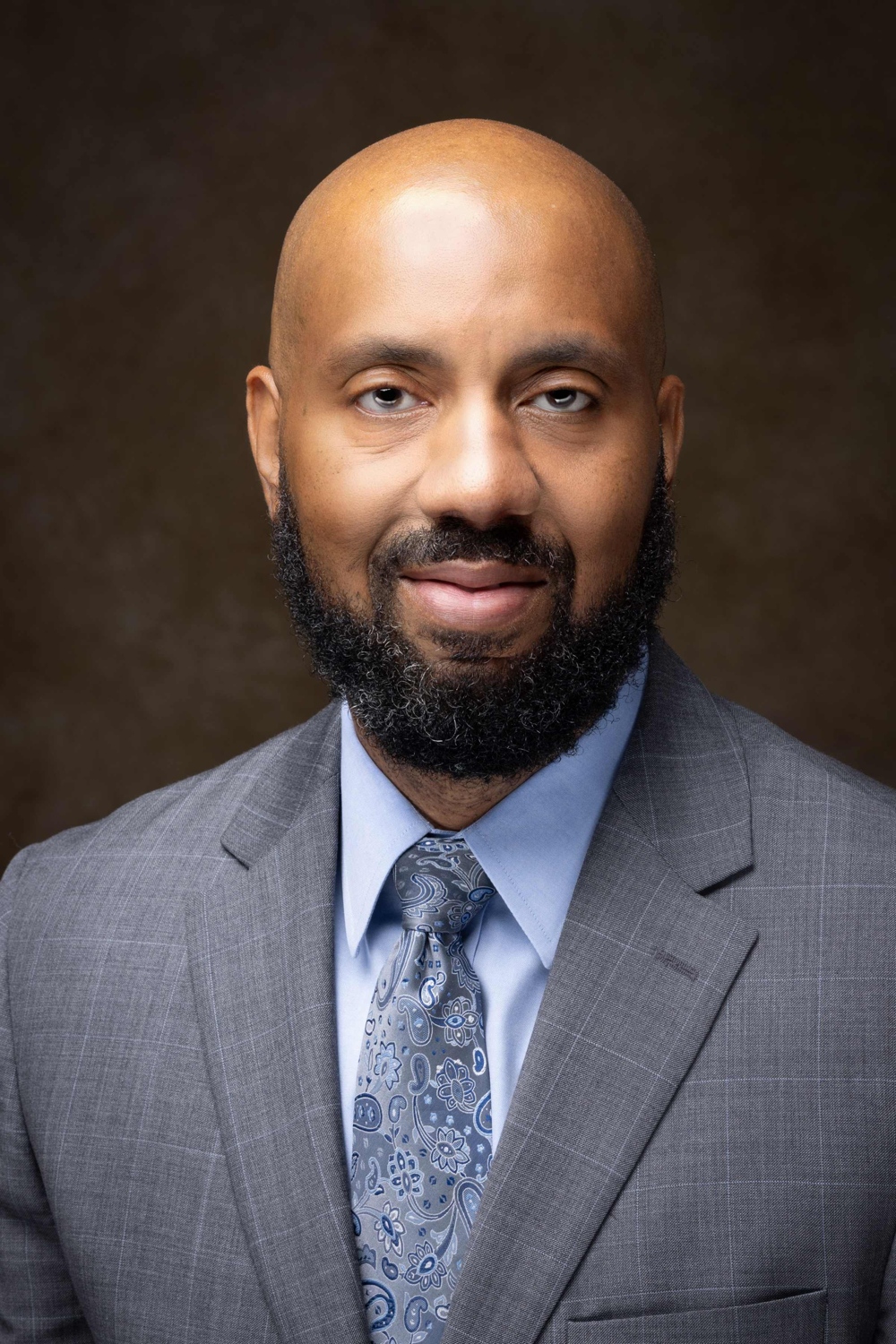 A distinguished man, in a business suite with a tie featuring a grey and blue abstract floral design.