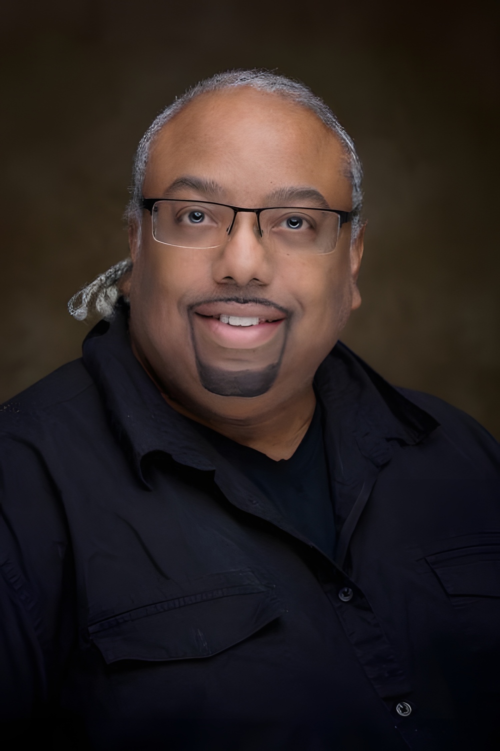 Dr. Raynor smiling at the camera, in a black dress shirt.