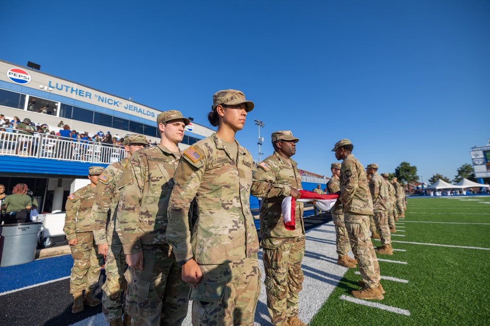 A number of soldiers standing at attention on a football field, two are in the middle of folding a flag.