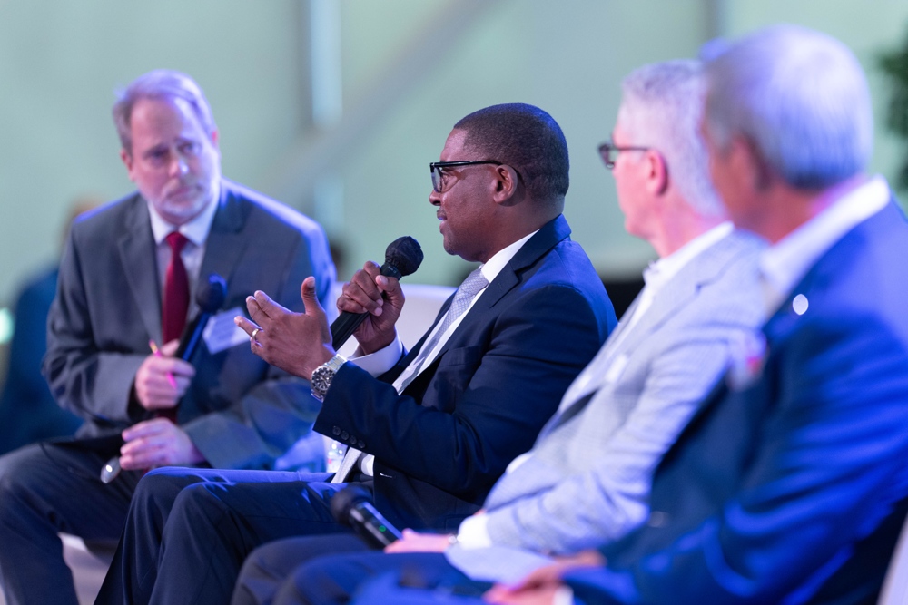A number of speakers on a panel, gentelman on the far left speaking.