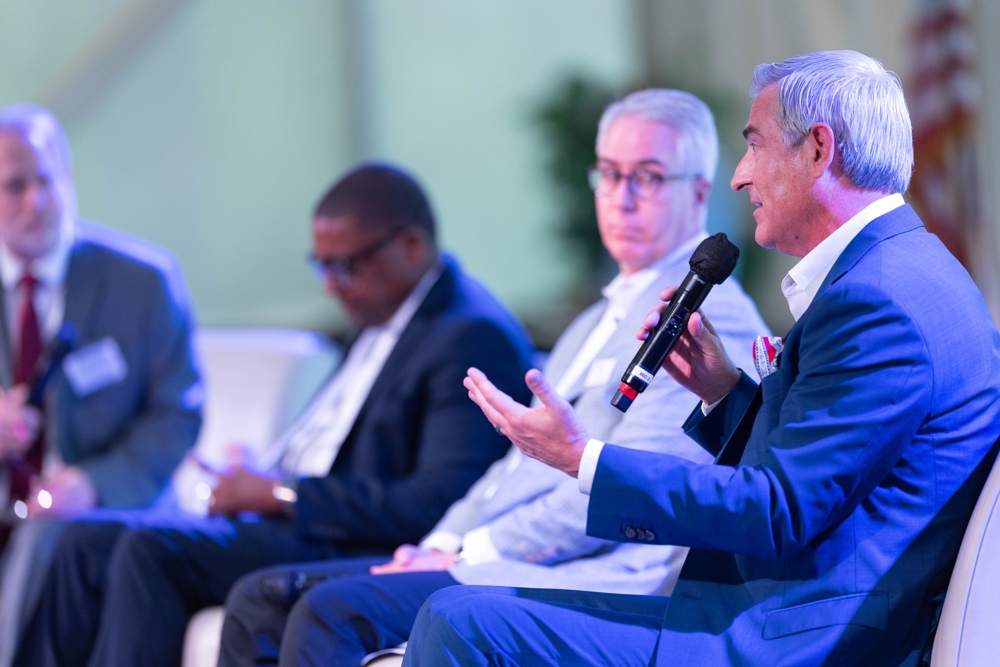 A number of speakers on a panel, gentelman on the far right speaking.