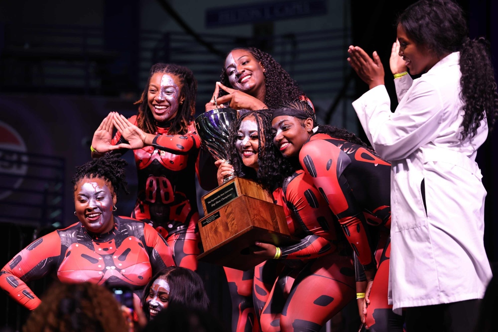 Performers in red and black jump suits, proudly displaying an award.