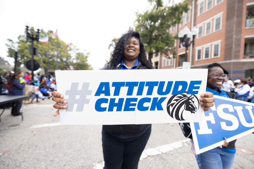 A student holding a sign that reads: Attitude Check