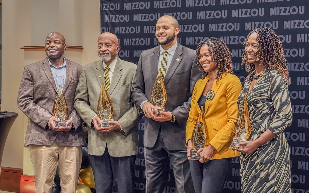 A number of men and women in formal attire, holding awards and smiling.