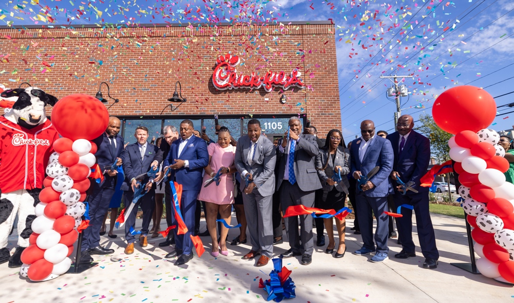The chancellor performing a ribon cutting in front of a resteraunt.
