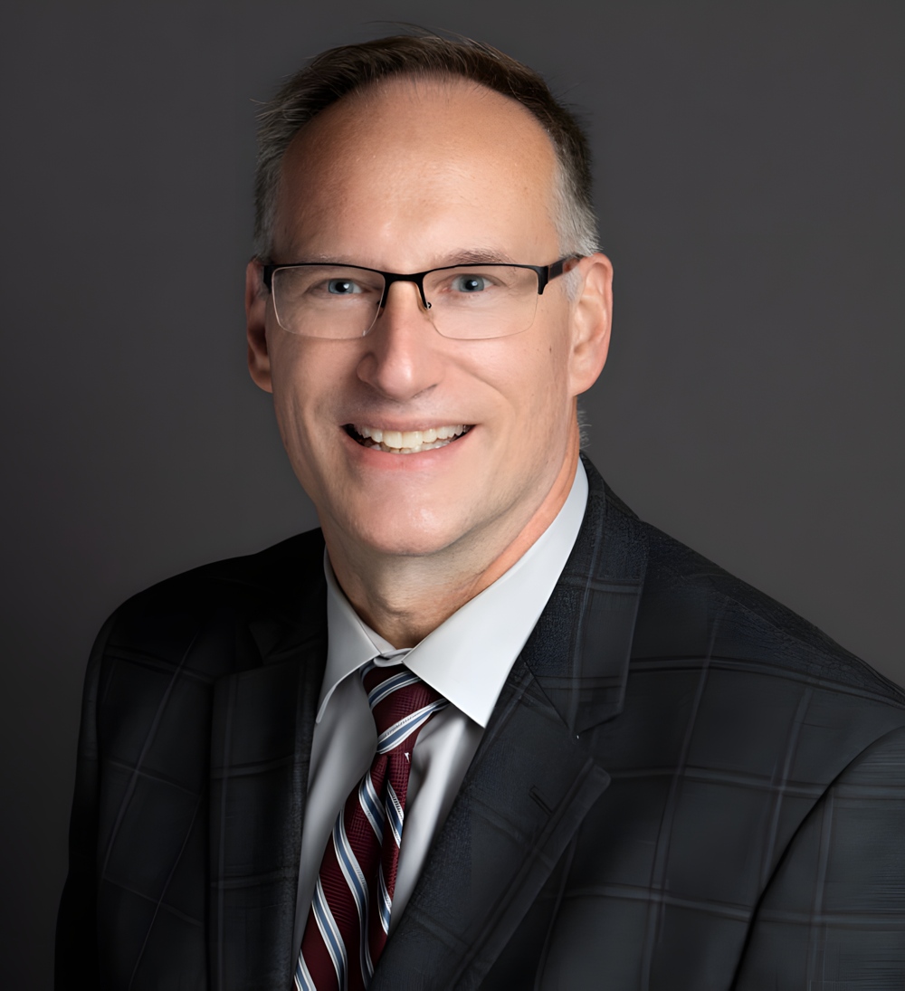 A smiling man in glasses with a profesisonal suit.